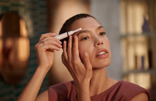 Woman with dark hair and brown eyes using Philips device to trim eyebrow hair.