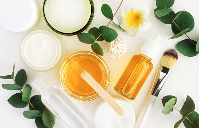 Arrangement of yellow wax in glass pot waxing and tools amidst floral decorations on white surface.