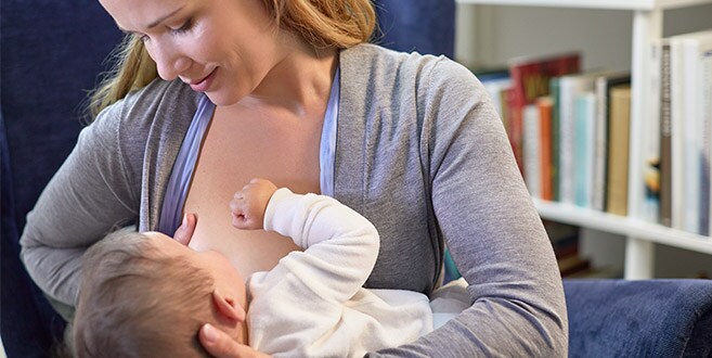 A mother shows the cross-cradle hold, breastfeeding while supporting baby with one arm and her breast with the other.