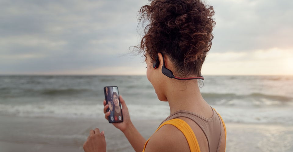 Athlete taking a call on the beach while using bone-conducting headphones