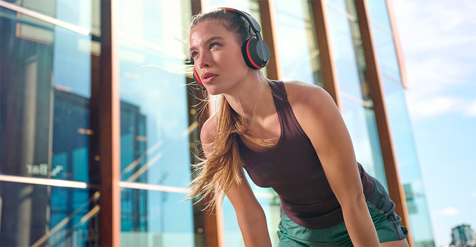 Woman wearing Philips A6219 headphones taking a break during an outdoor workout, standing in front of a modern glass building