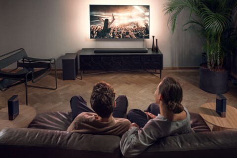 A couple using Fidelio B97 soundbar while watching a concert at home