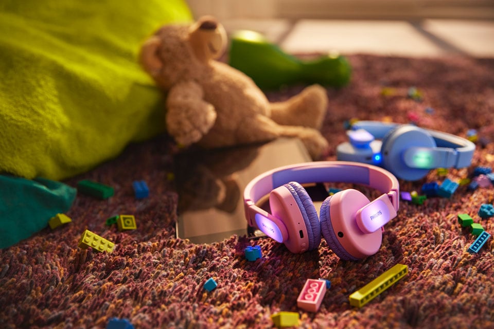 A blue and a pink kids headphones on the floor with toys