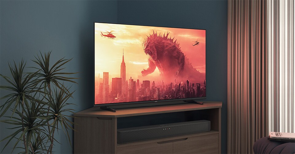 A Philips TV on a corner stand displays a Godzilla movie