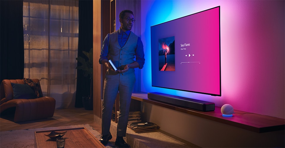 Person in a modern living room near a Philips Ambilight TV with music interface and Fidelio soundbar