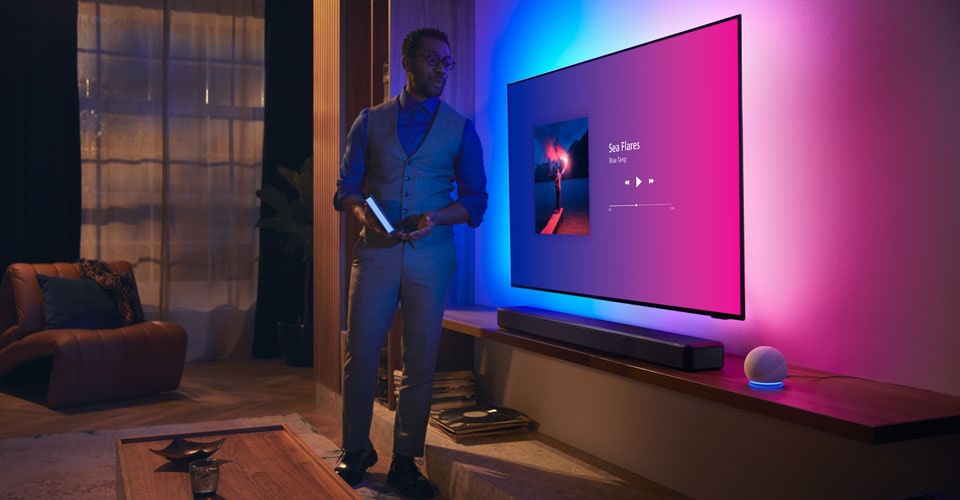 Person in a modern living room near a Philips Ambilight TV with music interface and Fidelio soundbar