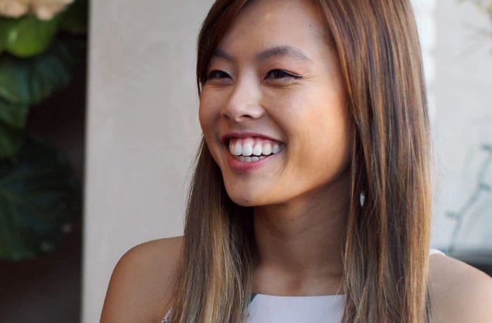 A young woman is smiling widely at something beyond the camera, revealing a set of bright white teeth. 