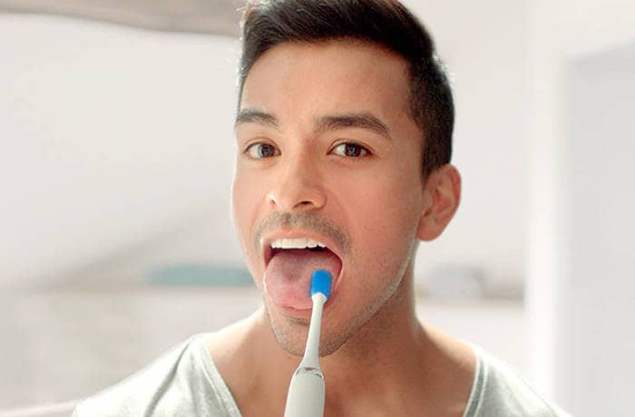 A man is looking towards the camera cleaning his tongue covering using a special Philips tongue brush.