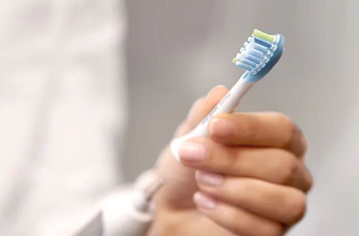 A person is reattaching the detachable brush head of a white electric toothbrush. 