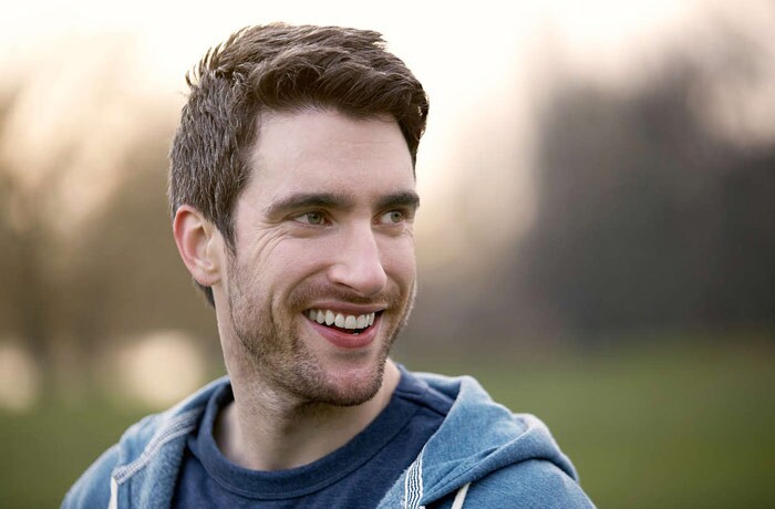 A young man has a wide smile on his face, revealing a set of symmetrical white teeth.