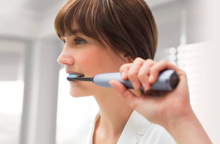 A woman brushes her teeth with a grey Philips Sonicare.