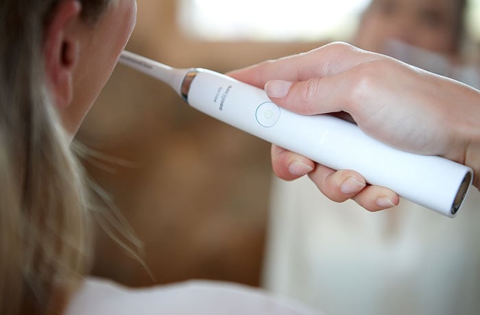 A close-up of a woman brushing her teeth using a white Philips Sonicare electric toothbrush.