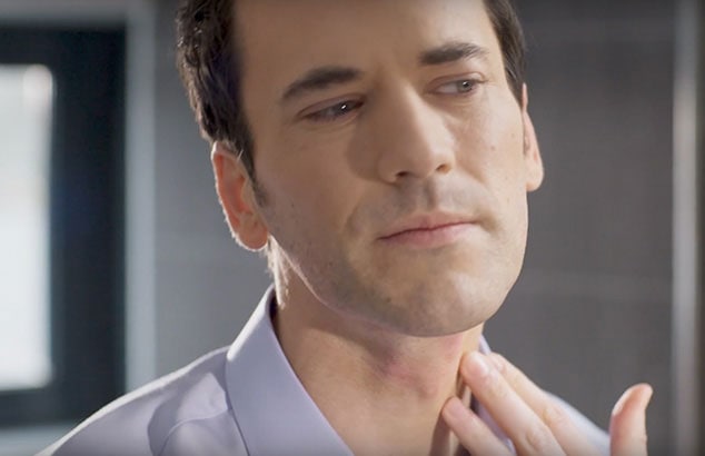A clean-shaven man placing his fingers against some red marks on his neck.