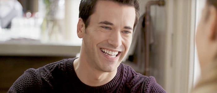 Close-up of clean-shaven smiling man in dark clothing.