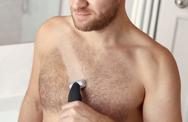 Close-up of a man’s hairy chest with stripe being shaven across by an electric shaver he is holding.