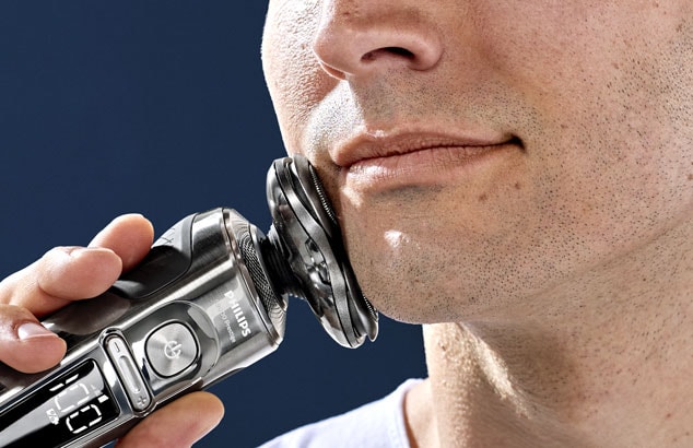Close-up of a man’s chin with very short stubble pressing an electric razor against his jaw.