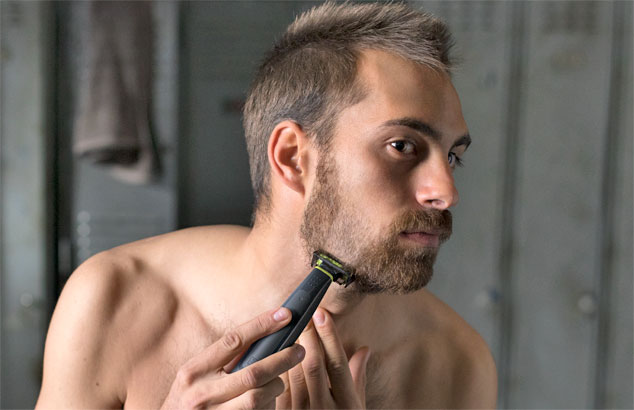 A man is trimming his scruffy beard down to a stubble using a trimmer with a special attachment.