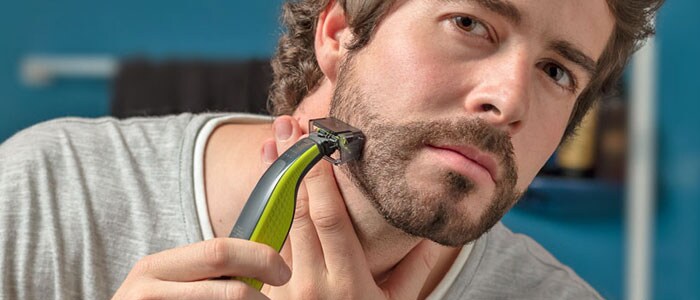 A man is marginally trimming down his beard using a trimmer with a special attachment.