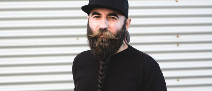 A man with a braided Viking beard – he is wearing black clothes and looking into the camera.