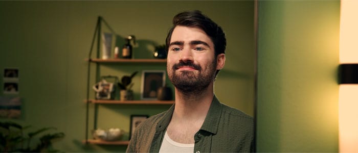 Man with dark hair and a natural, full beard smiles in the mirror in a room with a green background