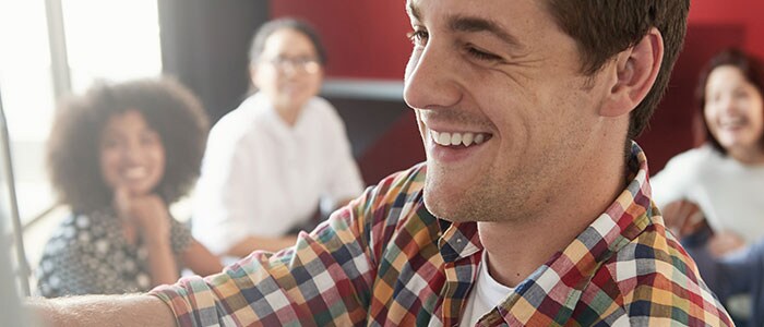 Close-up of a smiling man’s face, with four people out-of-focus in the background.