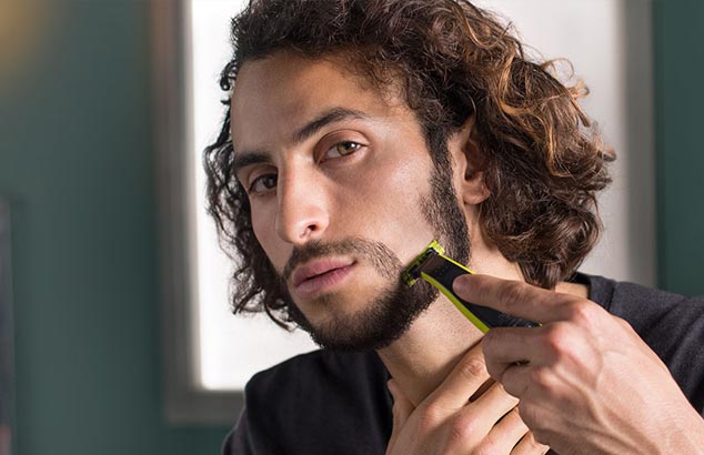 A man is closely shaving a panel of his stubbly beard, resulting in a shaped moustache.