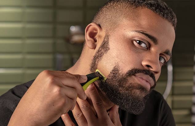 A man is vertically shaving his short beard from his cheek to his jawline, resulting in a clean-shaven patch.