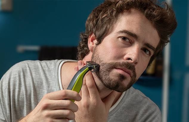 A man is trimming his short chin beard using a trimmer with a special attachment.