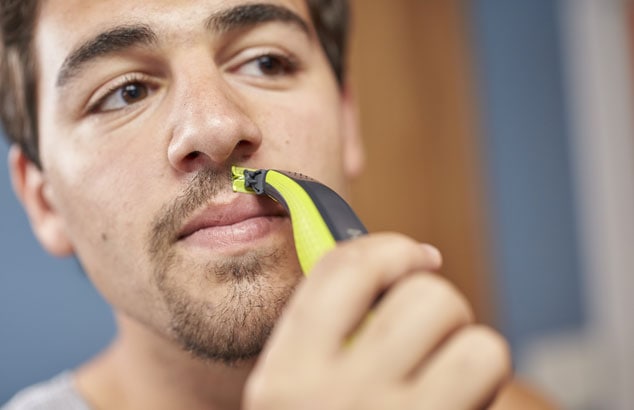 Man with brown hair and eyes using Philips OneBlade to shape his goatee beard above his lips.