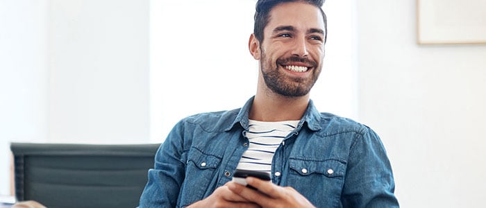 A man wearing a shirt with beard stubble holds a phone while smiling.