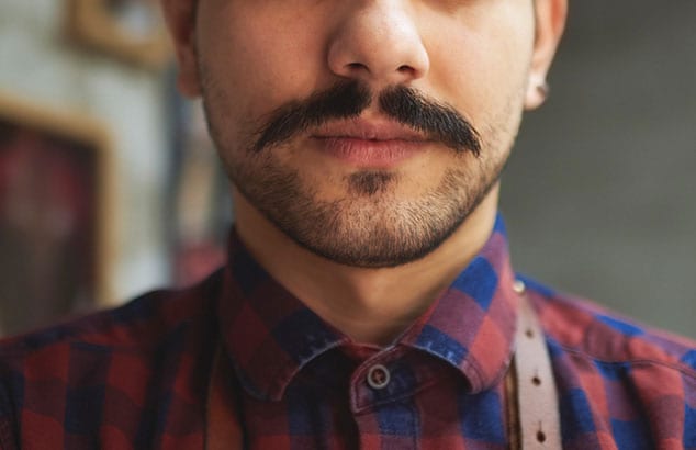 Closeup of a man with a nicely trimmed dark moustache wearing a plaid shirt. 