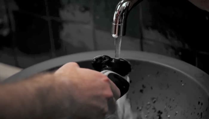  Close up of a man running an electric razor under a running tap to clean it.
