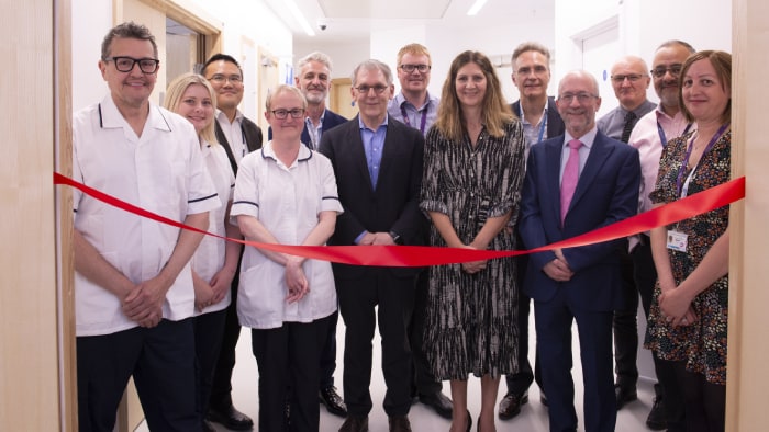 image shows staff at Leeds Hospital celebrate the opening of the MRI simulator by cutting a red ribbon.
